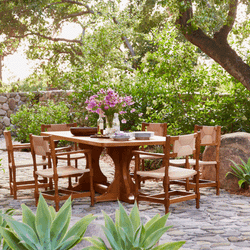 A lakeside outdoor scene under a pergola with a long dining table with chairs and a banquette on the right, and a seating group of four armchairs on the left.
